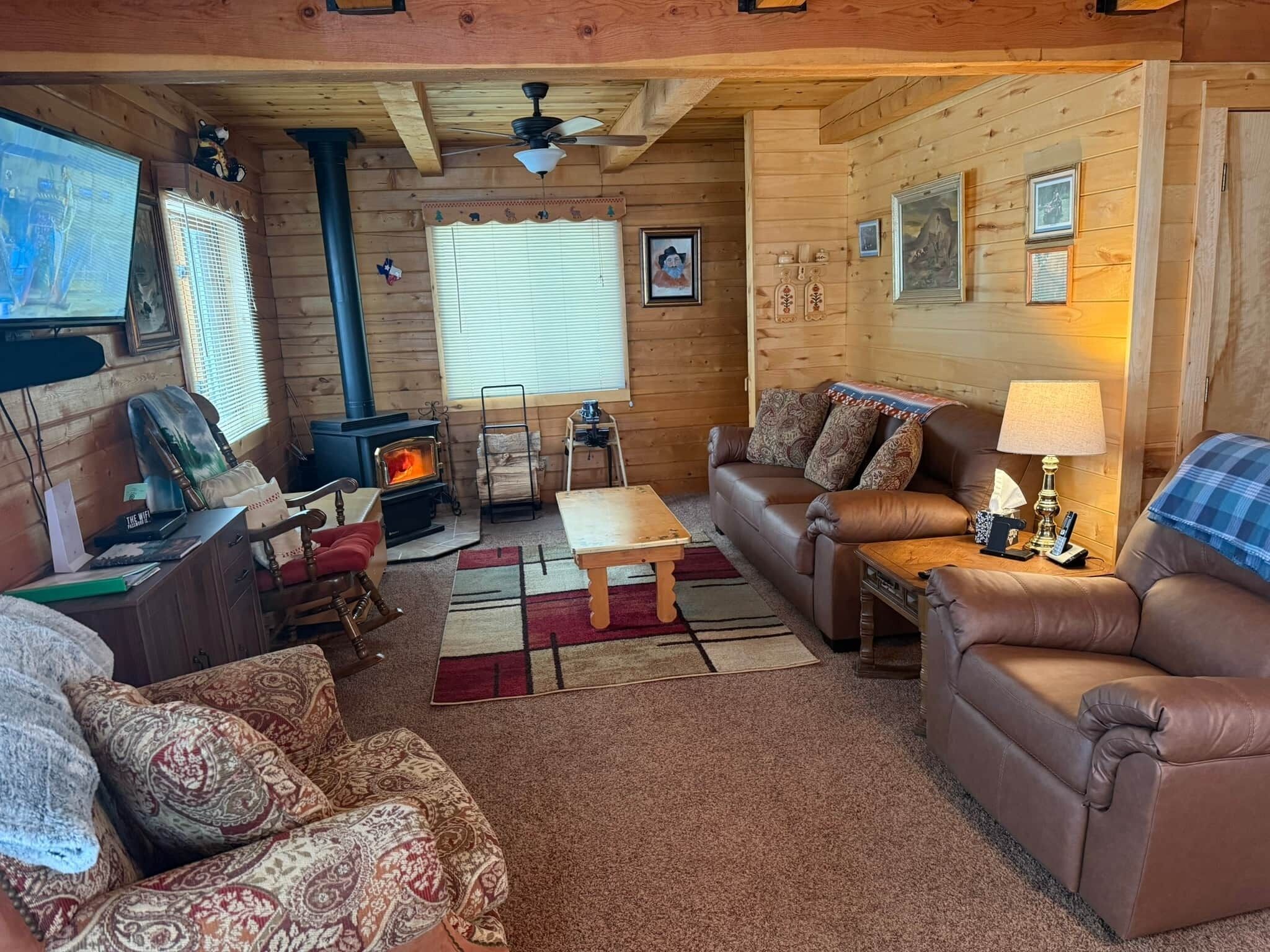 Un intérieur de chalet chaleureux avec une cheminée, des canapés en cuir, un plafond en bois et un téléviseur.