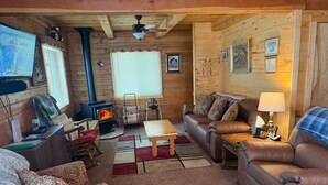 Ein gemütliches Blockhaus-Interieur mit Kamin, Ledersofas, Holzbalkendecke und Fernseher.