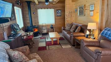 Un intérieur de chalet chaleureux avec une cheminée, des canapés en cuir, un plafond en bois et un téléviseur.