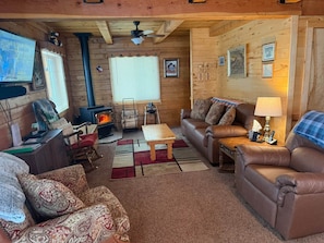 Ein gemütliches Blockhaus-Interieur mit Kamin, Ledersofas, Holzbalkendecke und Fernseher.