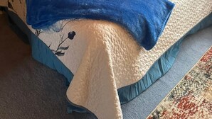 Ein gemütliches Schlafzimmer im Dachgeschoss mit Holzbalkendecke, einem Bett mit floralem Bettzeug und einem Gemälde an der Wand.
