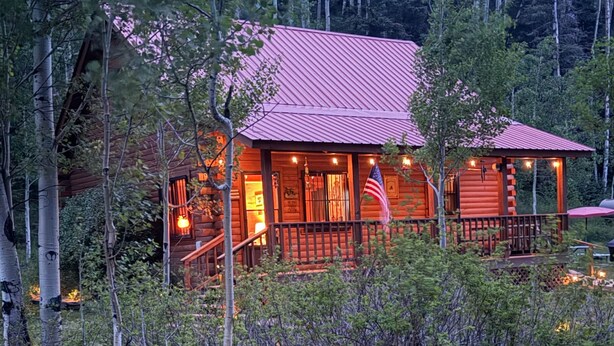 Eine Blockhütte mit rotem Dach, umgeben von Wald, mit Veranda und kleiner Terrasse.