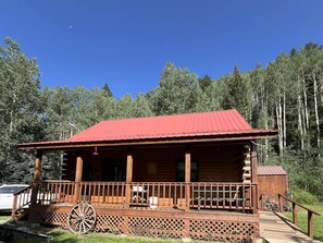 A wooden cabin with a red roof, a porch with a wooden railing, and a wheelbarrow.