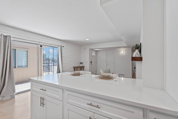 A modern kitchen with white cabinetry, a large island, and a dining area with a table set for two. - Summer Retreat with Pool & Views - Sleeps 8! (Tucson)