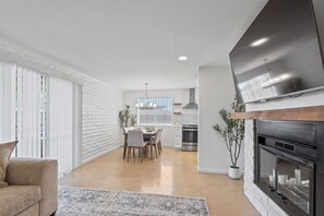 A modern living room with a fireplace, dining area, and kitchen. - Summer Retreat with Pool & Views - Sleeps 8! (Tucson)