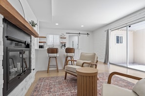 A modern living room with a fireplace, two bar stools, a sofa, and a round wooden table. - Summer Retreat with Pool & Views - Sleeps 8! (Tucson)