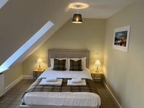 A bedroom with a sloped ceiling, a bed with white linens, two bedside lamps, and a painting on the wall. - Ancluaran (The Thistle) newly renovated one bedroom house 2+2 (Fort Augustus)