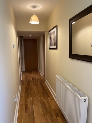 A hallway with wooden flooring, a radiator, a pendant light, and a framed picture on the wall. - Ancluaran (The Thistle) newly renovated one bedroom house 2+2 (Fort Augustus)