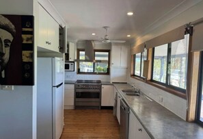 A modern kitchen with white cabinets, stainless steel appliances, and large windows providing natural light.