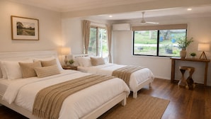 Quarto com duas camas, janela, ventilador de teto e mesa de cabeceira com abajur.