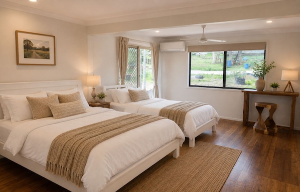 A bedroom with two beds, a window, a ceiling fan, and a bedside table with a lamp.