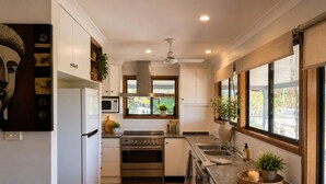 Uma cozinha moderna com armários brancos, eletrodomésticos de aço inoxidável, uma janela com vista para o verde e um ventilador de teto.