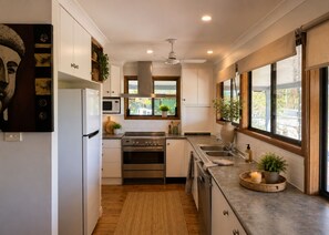 A modern kitchen with white cabinets, stainless steel appliances, a window with a view of greenery, and a ceiling fan. - Scenic Country Escape Peaceful 4BR Farm Stay (Nabiac)