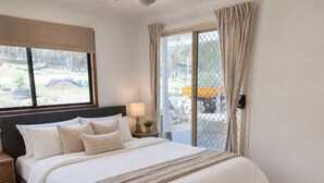 A bedroom with a large bed, a nightstand, a lamp, and a view through a sliding door.