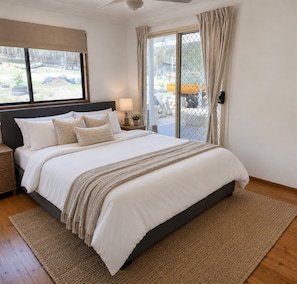 A bedroom with a large bed, a nightstand, a lamp, and a view through a sliding door.