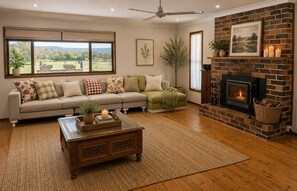 A living room with a sofa, a fireplace, a coffee table, and a view of the outdoors. - Scenic Country Escape Peaceful 4BR Farm Stay (Nabiac)