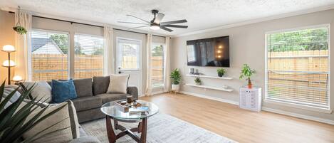 A modern living room with a sofa, coffee table, TV, and large windows.