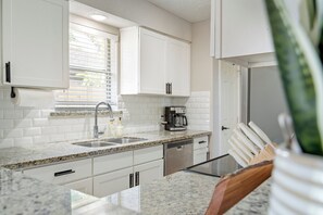 Eine moderne Küche mit weißen Schränken, Granit Arbeitsplatten, einem eingebauten Geschirrspüler und einer Kaffeemaschine.