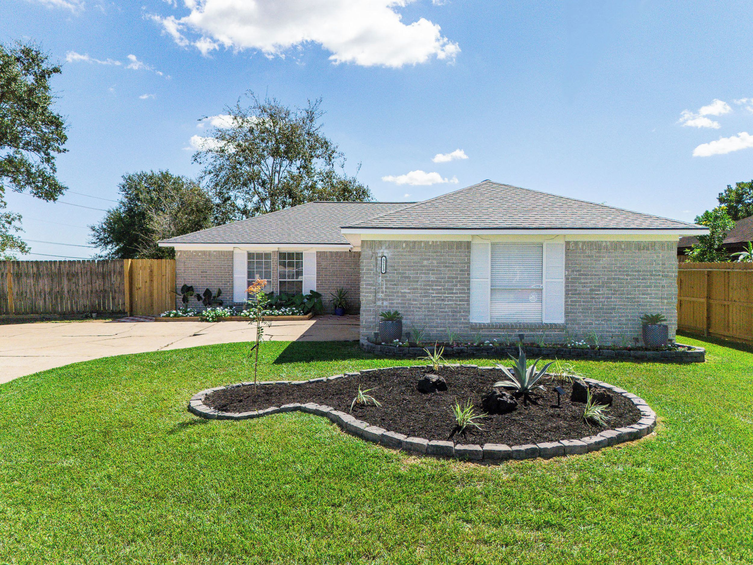 A residential house with a brick exterior, a front yard with a landscaped garden, and a wooden fence.