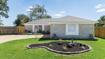 A residential house with a brick exterior, a front yard with a landscaped garden, and a wooden fence.