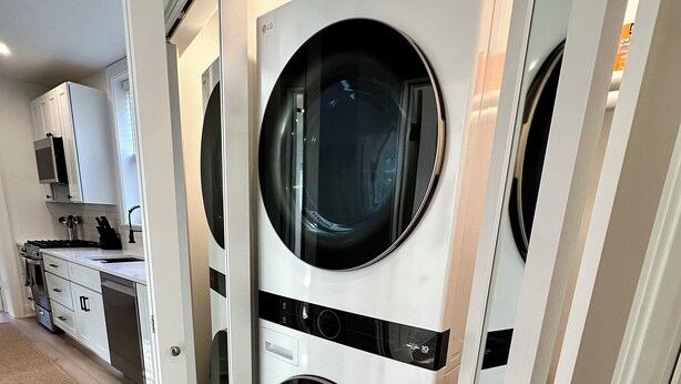 A laundry room with two front-loading washing machines, a kitchen area with white cabinets, and a wooden floor.