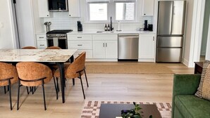 A modern kitchen with white cabinets, stainless steel appliances, a dining area with a marble table, and a green sofa.