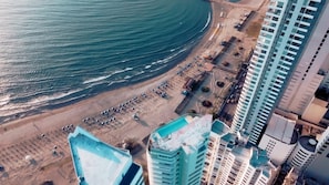 Vista aérea de una zona costera con playa, estacionamiento y edificios de gran altura.