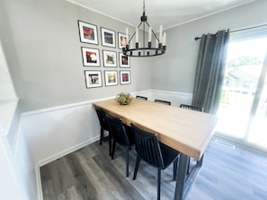 Un coin repas avec une table en bois, des chaises noires, un lustre et des tableaux encadrés accrochés au mur.