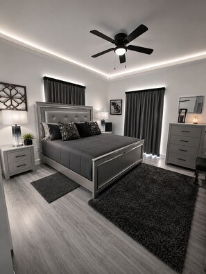 Un dormitorio moderno con cama, mesitas de noche, ventilador de techo y cómoda.