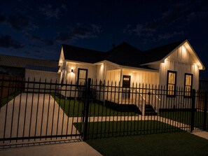 A two-story house with a front porch, a staircase leading to the entrance, and a fenced driveway.