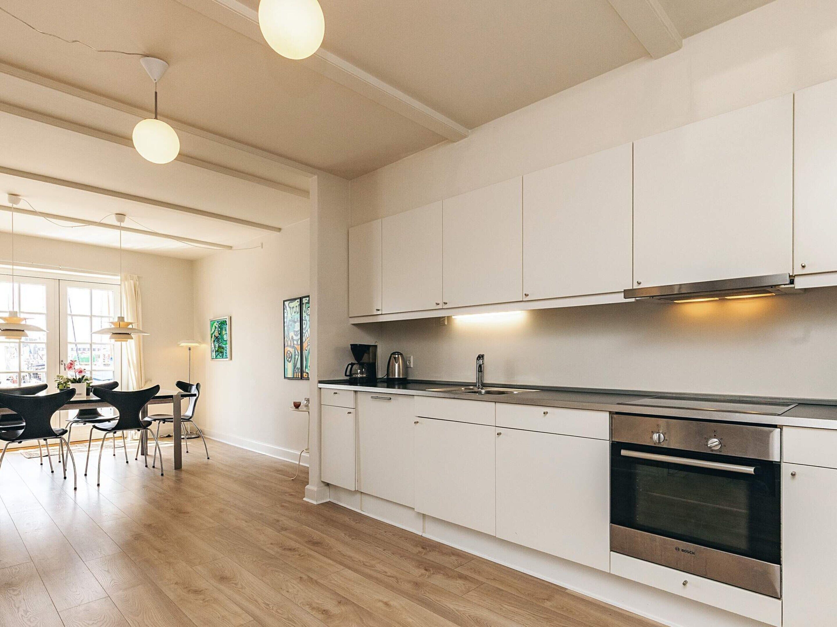 Una cocina moderna con armarios blancos, un horno Bosch e iluminación colgante.