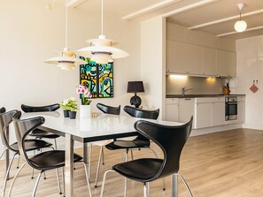 Un espace de salle à manger moderne avec une table blanche, des chaises noires et des luminaires suspendus.