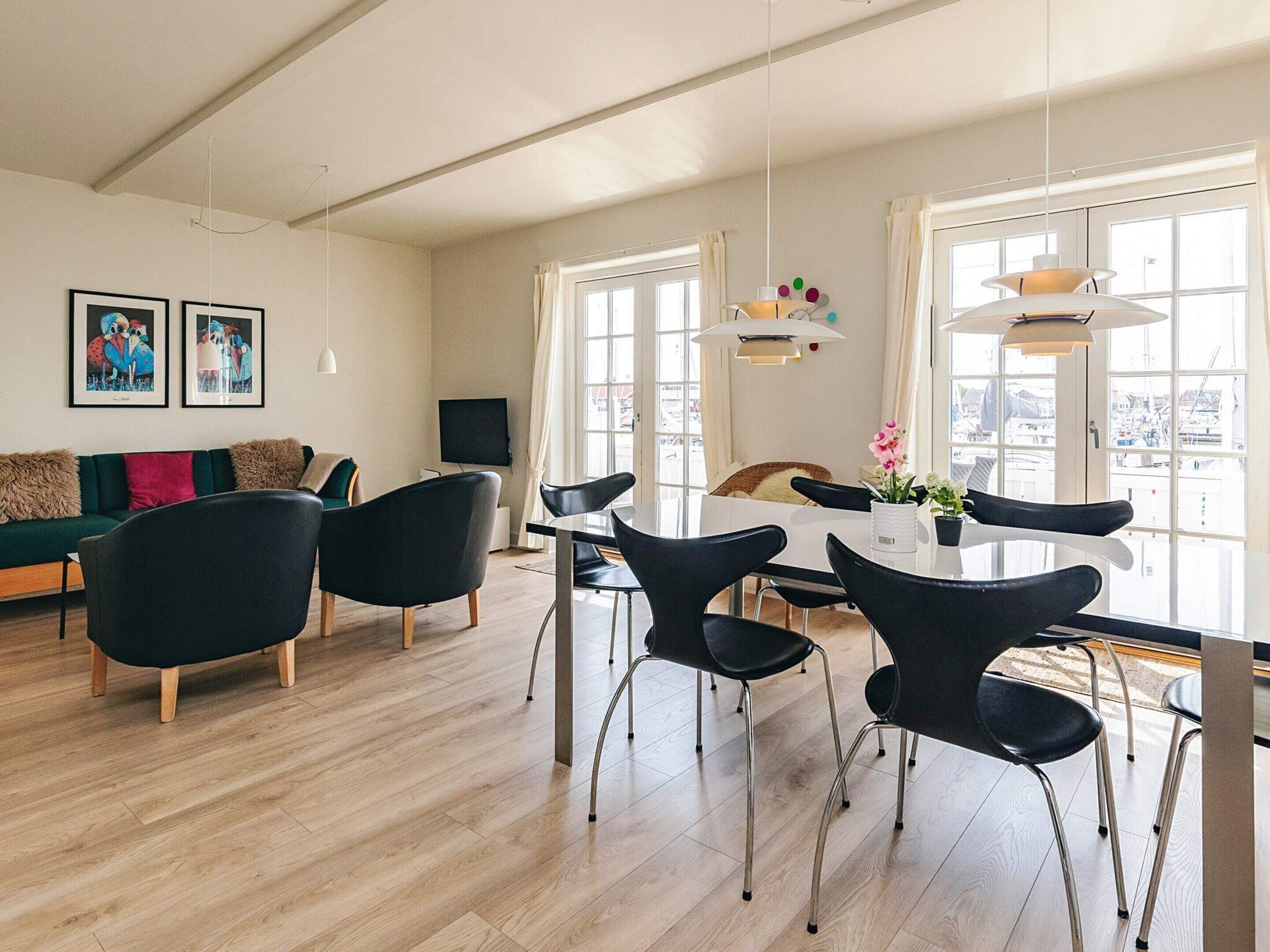 Una sala de estar moderna con comedor, piso de madera y ventanas grandes.