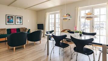 Una sala de estar moderna con comedor, piso de madera y ventanas grandes.