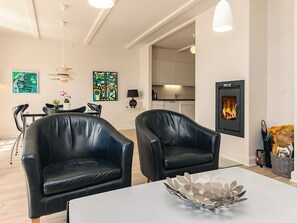 Uma sala de estar moderna com duas poltronas de couro preto, uma mesa branca com uma tigela metálica decorativa, uma lareira e arte abstrata nas paredes.