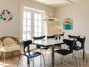 Un espace repas avec une table en verre, des chaises noires et des luminaires suspendus.