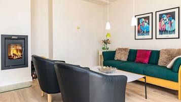 Un moderno salón con chimenea, un sofá verde, sillas negras y obras de arte en la pared.