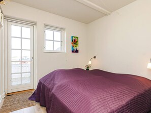Une pièce avec un lit, une porte, une fenêtre et une lampe fixée au mur.
