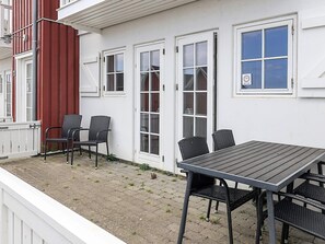 Une terrasse avec une table et des chaises, un mur rouge et des portes blanches.
