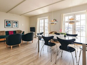 Un salon moderne comprenant un coin repas, de grandes fenêtres et un téléviseur à écran plat.