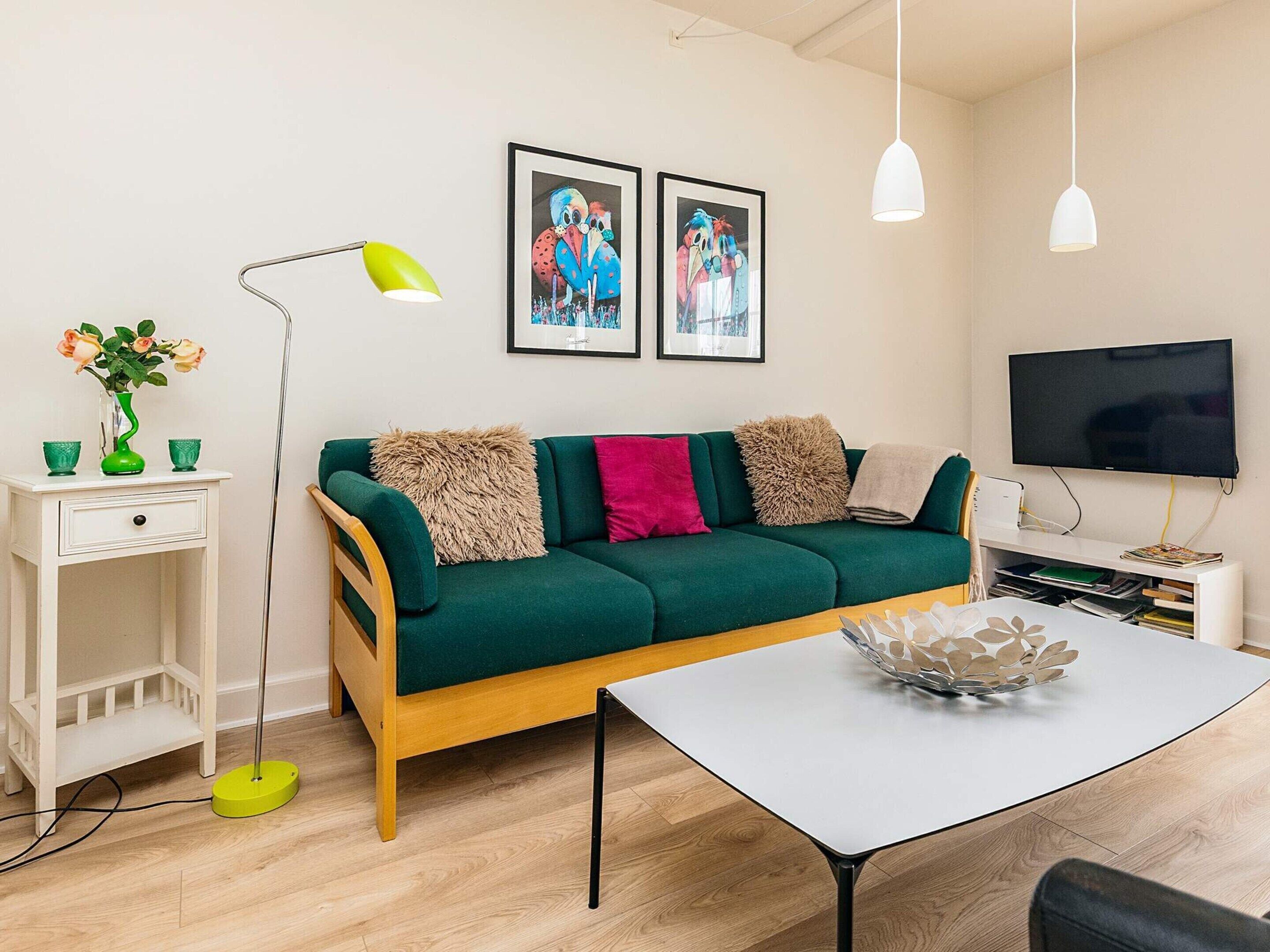 Un salon moderne avec un canapé vert, une table basse blanche, un téléviseur et une œuvre d’art encadrée accrochée au mur.