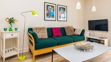 Una sala de estar moderna con un sofá verde, una mesa de centro blanca, un televisor y una obra de arte enmarcada en la pared.