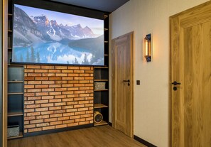 Ein Zimmer mit Kamin aus Backsteinen, Holztüren und einem großen Bildschirm, der eine Berglandschaft zeigt.
