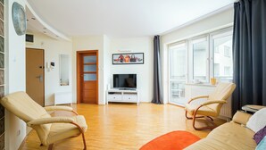 Een woonkamer met een bank, twee fauteuils, een televisie en een raam met gordijnen.