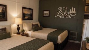 Een hotelkamer met twee bedden, een nachtkastje met lamp, een muur met het bord 'ON THE LAKE' en ingekaderde foto's.