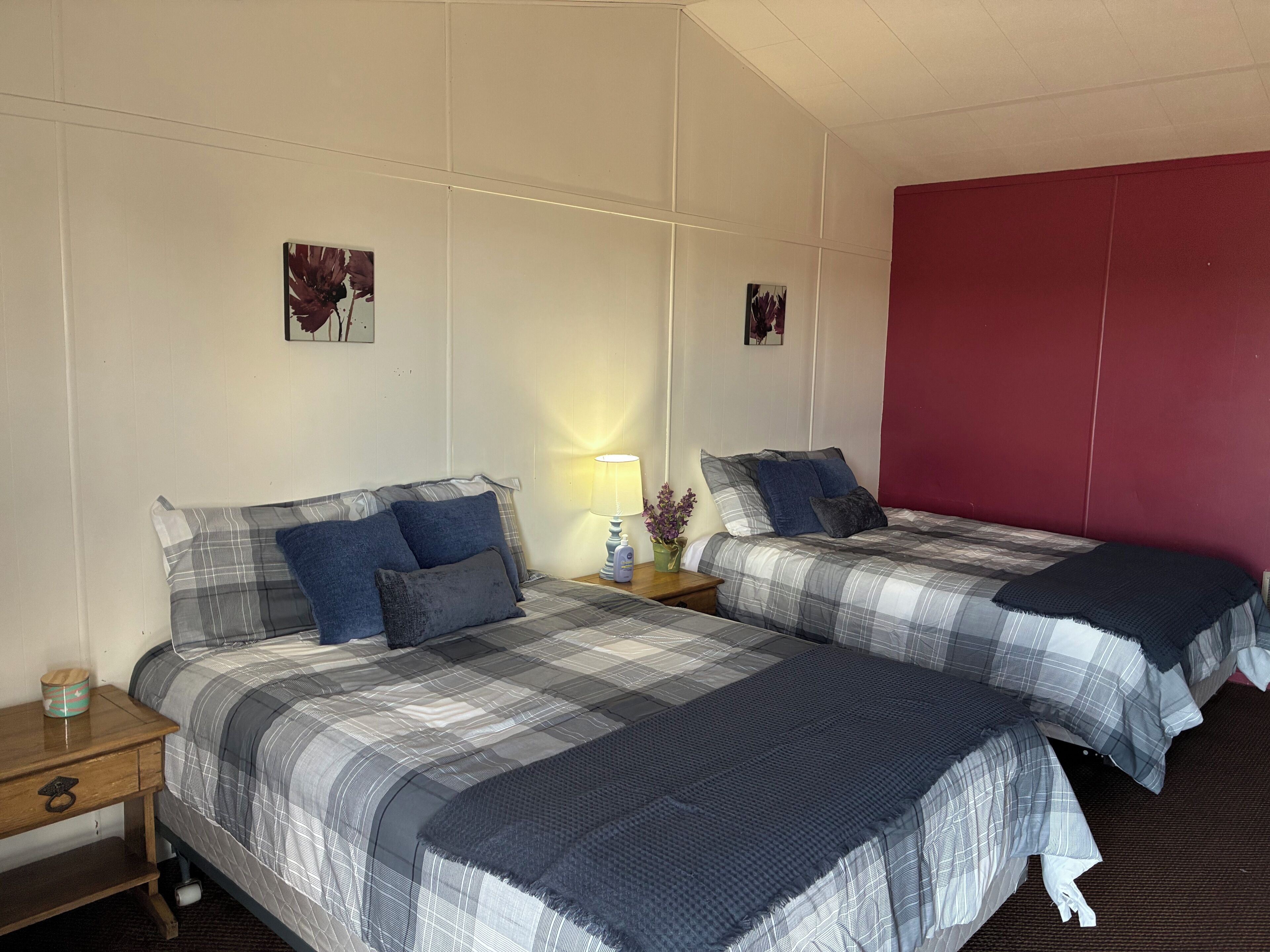 A hotel room with two beds, a nightstand, a lamp, and a red accent wall.