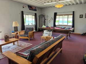 A room with a pool table, a sofa, a chair, a lamp, and a television on the wall. - Mesa View Lodge Resort (Lewellen)