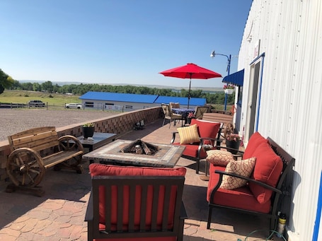 A patio area with outdoor seating, a fire pit, and a view of a building with a blue roof.. Mesa View Lodge Resort