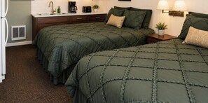 Habitación con dos camas, una mesita de noche, cafetera, una planta y una lámpara de pared.