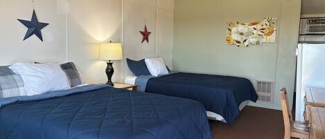 A hotel room with two beds, a desk, a lamp, and a refrigerator.